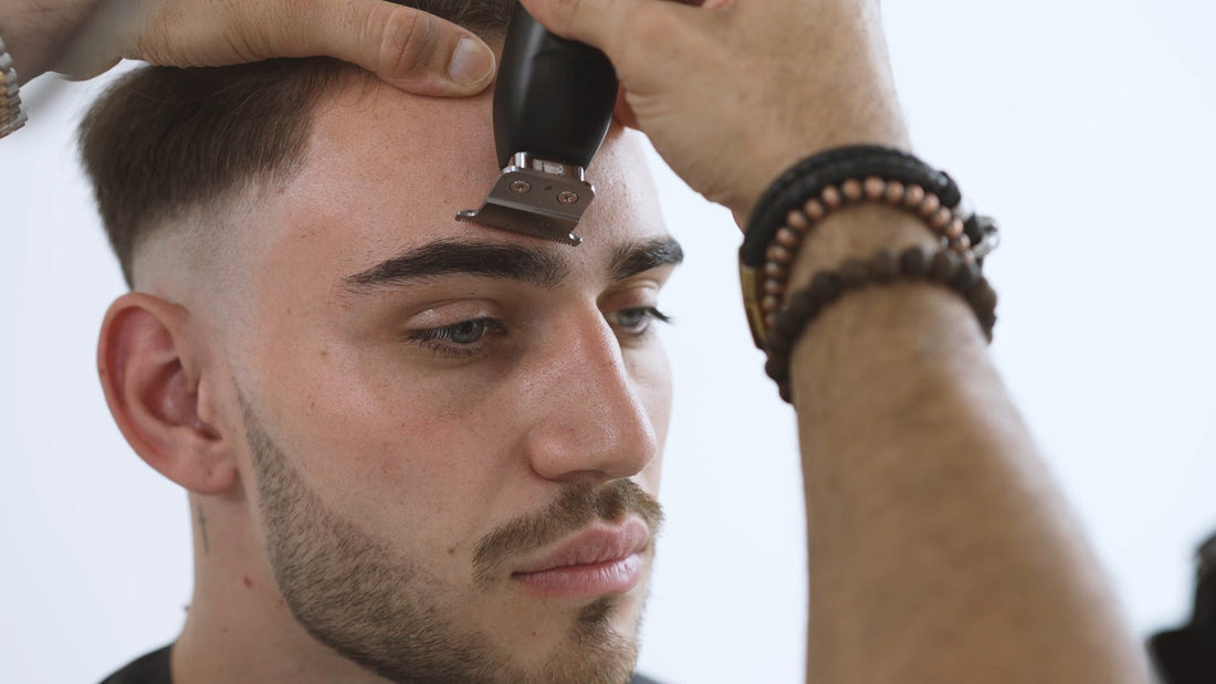 Barber lining up a client's forehead hairline with a T-blade trimmer